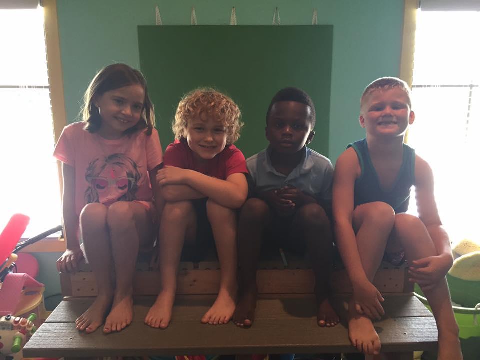 A group of kids sitting on top of a wooden bench.