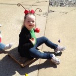 A little girl sitting on the ground wearing a bug costume.