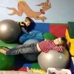 Two children are laying on exercise balls in a room.