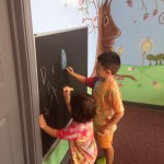 Two children are playing with a chalkboard.