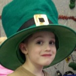 A young boy wearing a green hat and smiling.