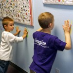 Two young boys playing with magnets on a wall.