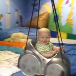 A baby is sitting in a swing on the bed.