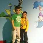 Two boys standing in front of a wall with dr seuss characters on it.