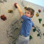 A boy is climbing on the wall of an indoor rock gym.