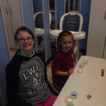 Two children sitting at a table with cups of paint.