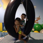 Two children are playing on a tire swing.