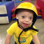 A little boy wearing a yellow helmet and smiling.