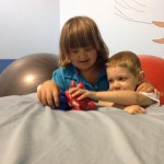 Two children playing with a toy on the bed.