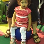 A little girl sitting on top of an exercise ball.